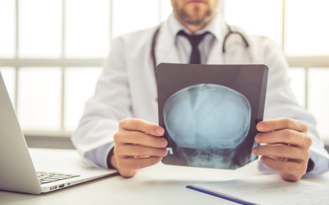 Handsome medical doctor in white coat is examining radiograph while working in his office