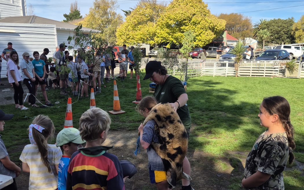 The kids choose between a dead pig or rabbit, which they carry on their back round the course, jumping hay bales and pallets, weaving between cones and fences, and then clearing the creek.