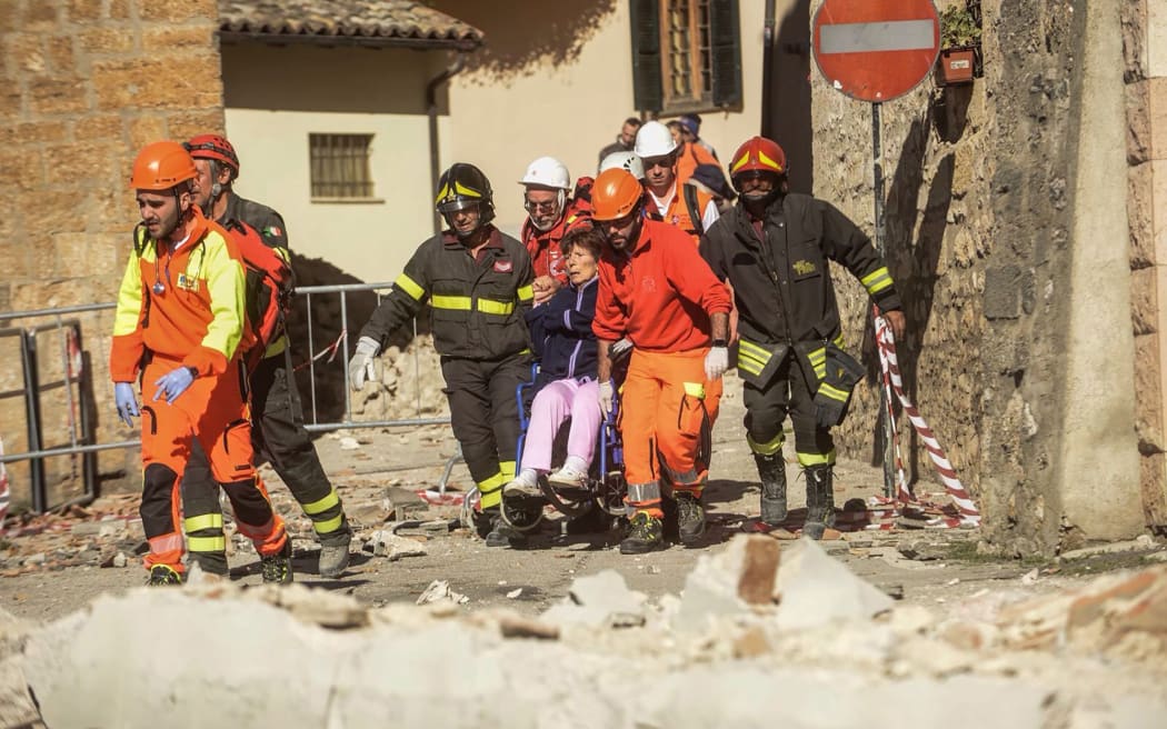 Firefighters and rescuers in Norcia carry a woman on a wheelchair after the quake.