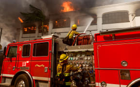 A firefighter on top of a fire truck directs water toward the flames, attempting to prevent further spread of the fire in Pacific Palisades, California, on January 8, 2025. The most destructive fires in Los Angeles history have killed at least five people, destroyed thousands of structures, and forced some 180,000 people to evacuate. (Photo by Jason Ryan/NurPhoto) (Photo by Jason Ryan / NurPhoto / NurPhoto via AFP)