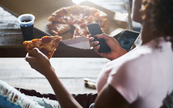 woman staying up late relaxing at home watching tv and eating pizza