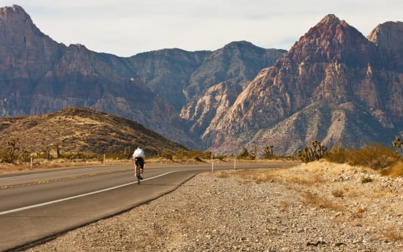 9750128 - a lone cyclist peddling up a desert highway toward distance mountains