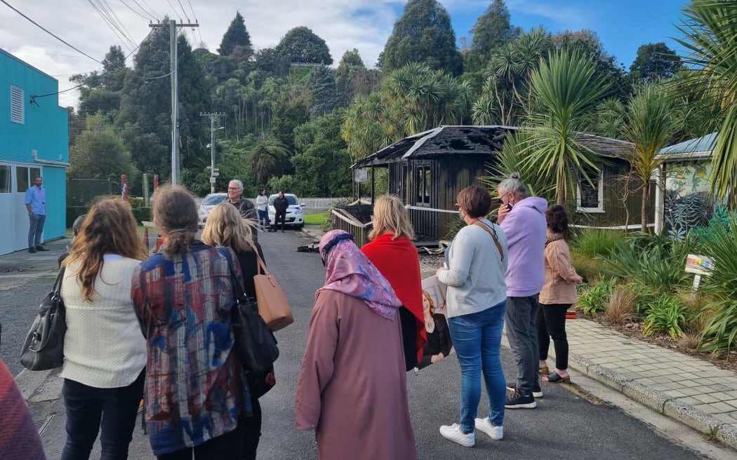 People stand around in the street outside the building as a press conference is given.