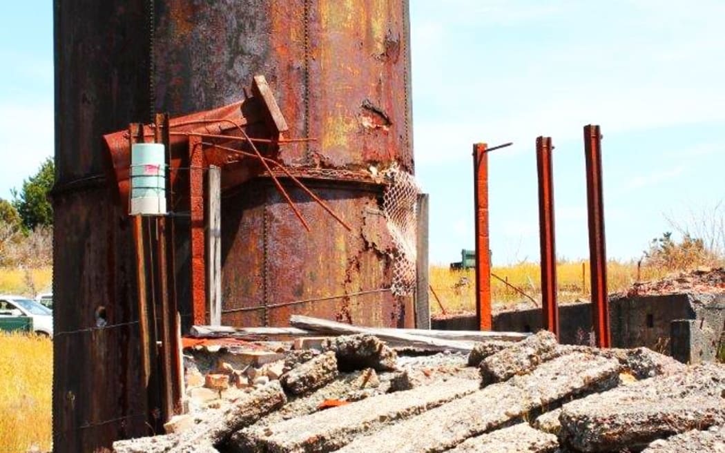 A rusty orange condensing tower at New Zealand's most toxic site, the historic Prohibition gold mine at Waiuta on the West Coast.  Surround but rusty metal and large lumps of broken concrete
