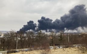 A picture taken on March 26, 2022 shows a religious statue as dark smoke rises from a fire following an air strike in the western Ukrainian city of Lviv.