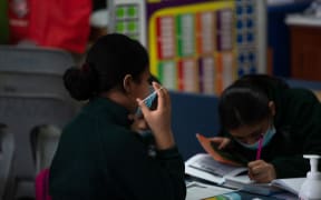 An Auckland child putting on her face mask at school.