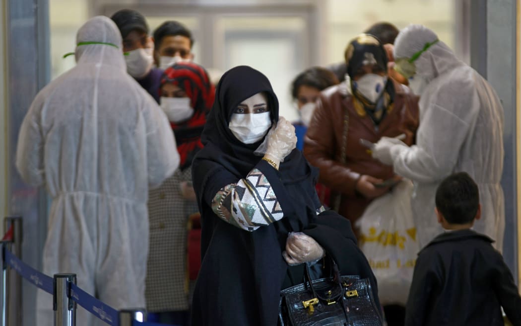 Medical staff in protective gears distribute information sheets to Iraqi passengers returning from Iran at Najaf International Airport on March 5, 2020. -