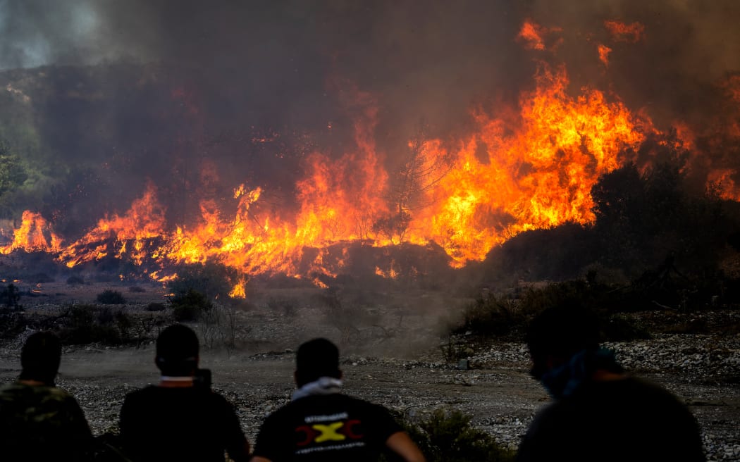 Locals watch the wildfires near the village of Vati, just north of the coastal town Gennadi, in the southern part of the Greek island of Rhodes on July 25, 2023. Some 30,000 people fled the flames on Rhodes at the weekend, the country's largest-ever wildfire evacuation as the prime minister warned that the heat-battered nation was "at war" with several wildfires and spoke of three difficult days ahead.
