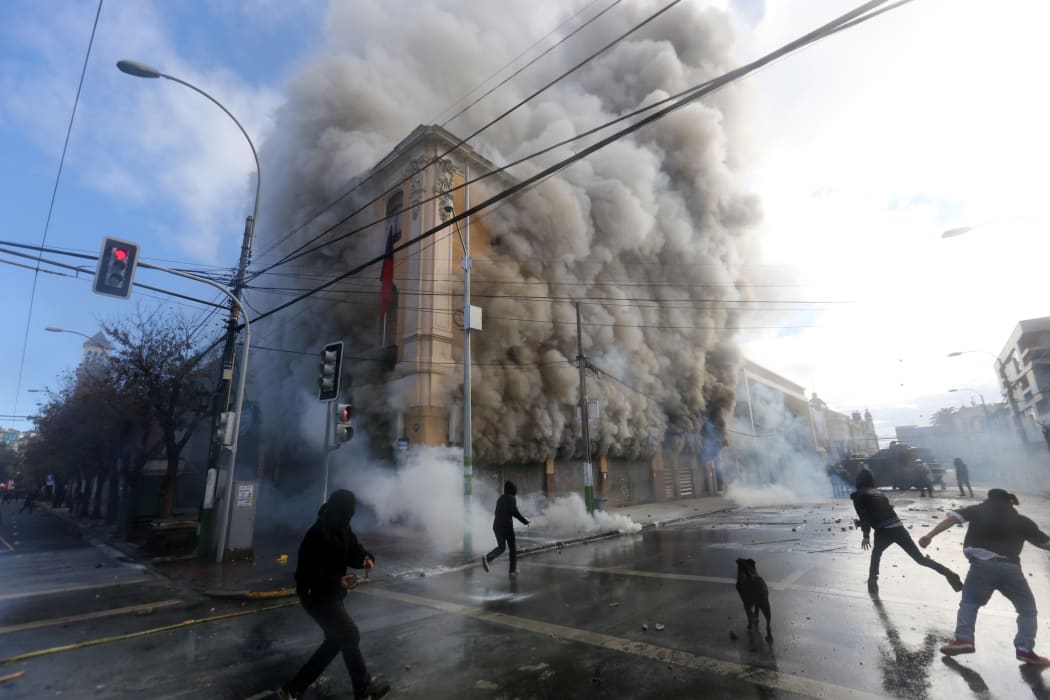 A security guard died when masked protestors burnt a pharmacy and supermarket.