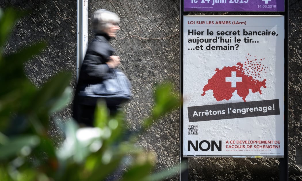 A woman walks past a campaign poster against toughening gun law in Switzerland and reading in French "Yesterday banking secrecy, today shooting... and tomorrow ? Let's stop the spiral!", on May 13, 2019, in Geneva.