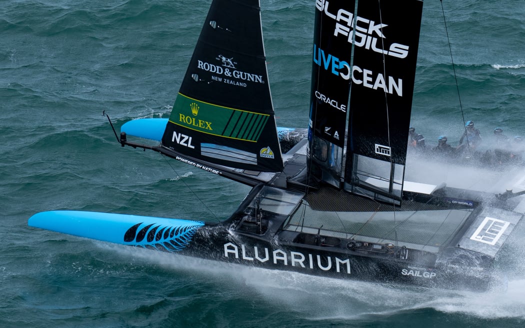 The Black Foils helmed by Peter Burling in action as they hit a wave during racing on Race Day 2.