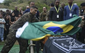 A military policeman of Special Police Operations- (BOPE) puts a Brazilian flag over the coffin of Heber Carvalho da Fonseca, a 39-year-old sergeant of the Special Police Operations Battalion (BOPE), following Brazil's bloodiest police raid, which left at least 119 people dead, in Rio de Janeiro, Brazil on October 30, 2025. The incident draws renewed attention to the city's controversial war against drug gangs entrenched in impoverished neighborhoods. (Photo by AFP)