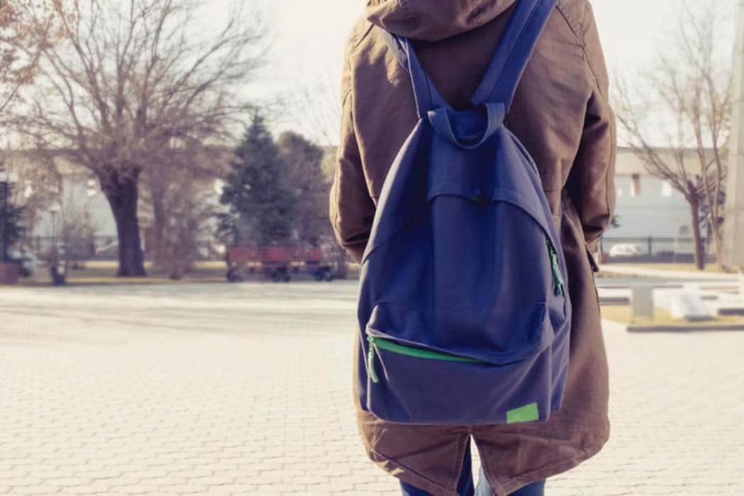 A photo of a teenager from behind showing her back pack and a school yard in the back ground