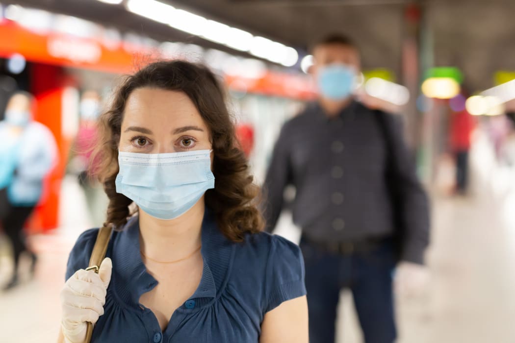 Person in medical mask and protective gloves waiting for train at subway station.