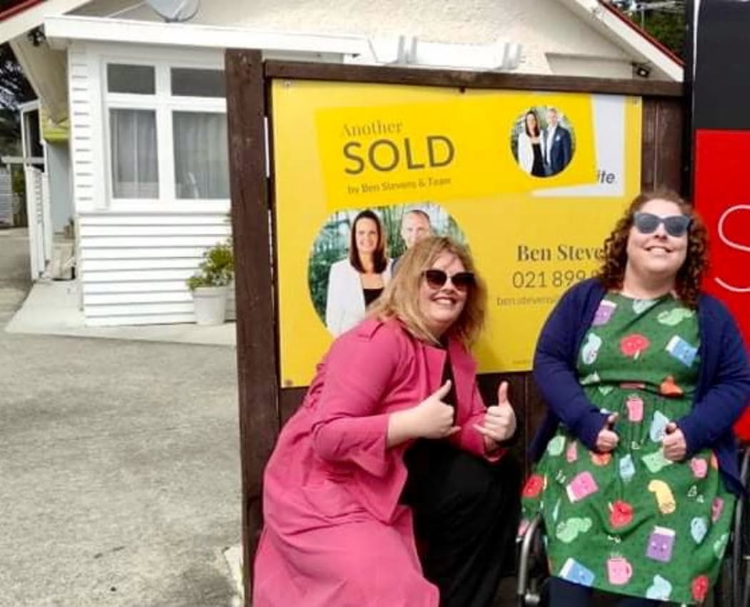 Erin Gough and Harriet Hamilton celebrate buying a home by posing in front of the sold sign