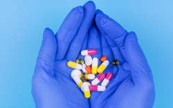 Different pills in hand in a medical glove on a blue background. Medicine. Treatment. Prevention