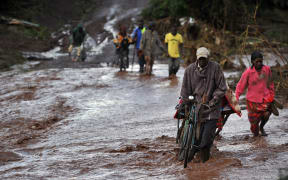 Villagers cross through receding waters at Solai after the banks of a dam burst its banks killing at least 41.