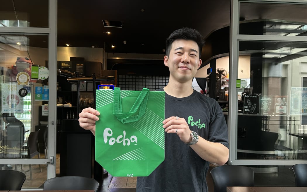 奥克兰中央商务区 Pocha 餐厅前厅经理 David Lee 手持外卖袋的照片。