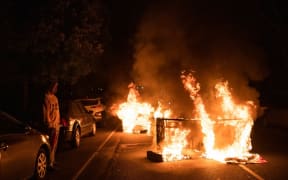 A man watches as a sofa, set on fire by protesters, burns in his street in West Philadelphia on October 27, 2020,  during a demonstration against the fatal shooting of 27-year-old Walter Wallace, a Black man, by police.