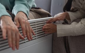 Family warming hands near electric heater at home, closeup.