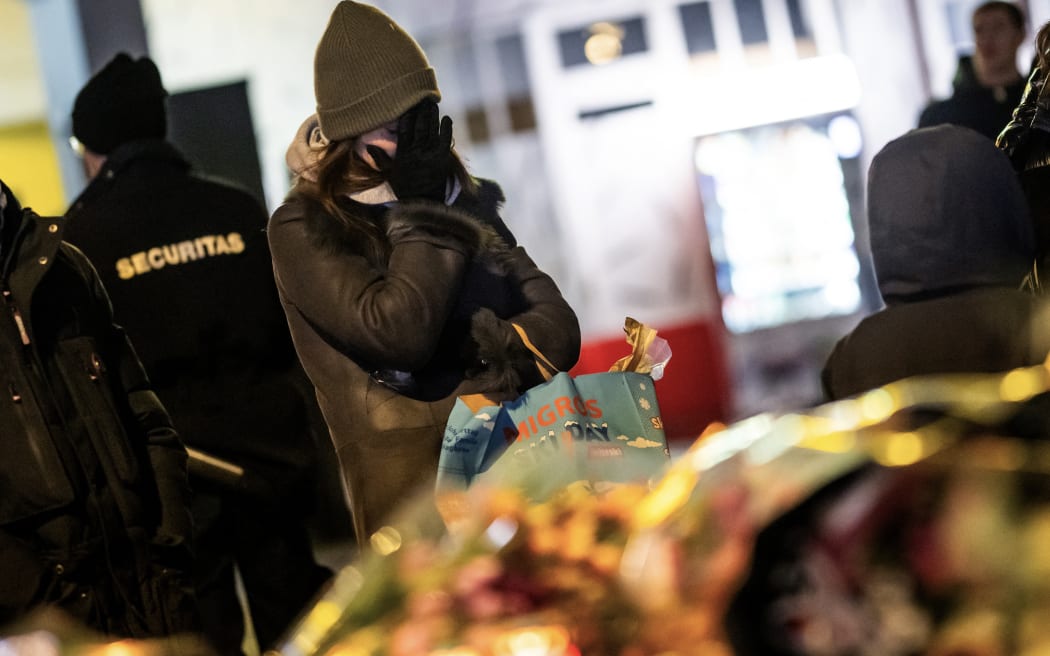 A mourner gestures in front of flowers and candles laid near the site where a fire ripped through a crowded bar during New Year's Eve celebrations in the Alpine ski resort town of Crans-Montana on January 1, 2026. Several dozen people are presumed dead and around 100 injured after a fire ripped through a crowded bar in the luxury Swiss ski resort of Crans-Montana, Swiss police said on January 1, 2026. Police, firefighters and rescuers rushed to the popular resort, which is set to host the Ski World Cup from January 30, after the fire broke out in the early hours of New Year's Day. (Photo by MAXIME SCHMID / AFP)