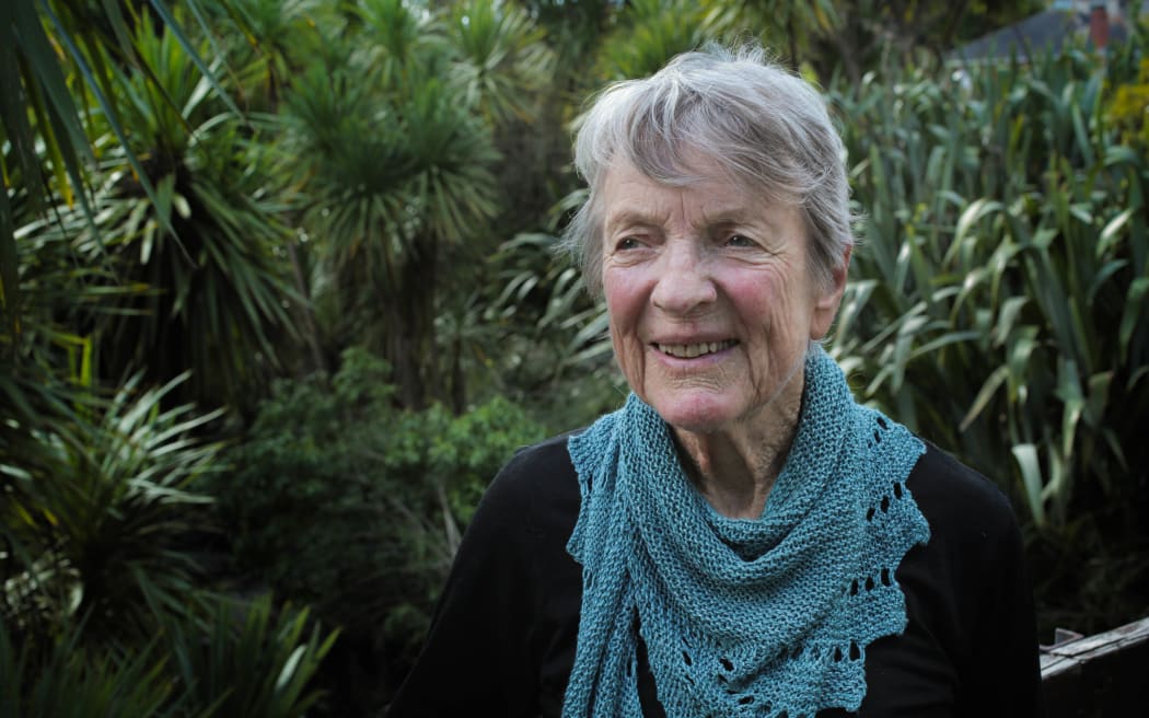 A head and shoulders portrait of Helen Haslam, an older woman with short grey hair, against a backdrop of native bush