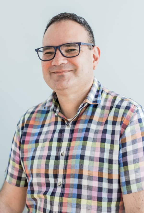 Ben Sedley - a man in glasses and a check shirt - smiles slightly at the camera.