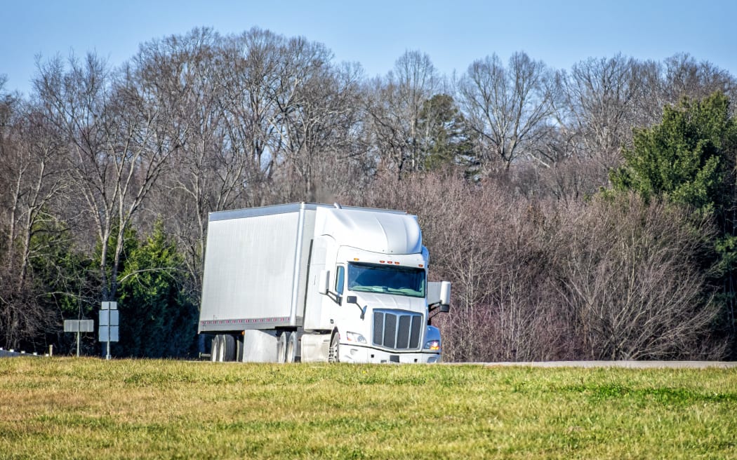 Horizontal shot of a generic white tractor trailer truck on a highway.