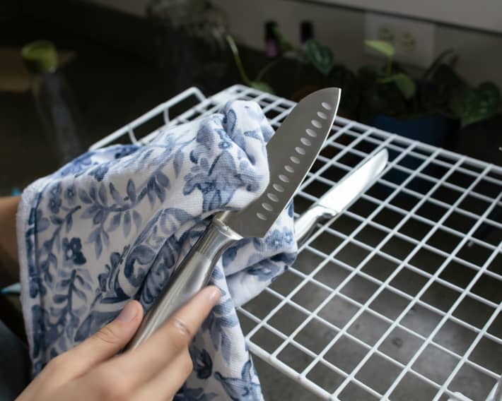 A person uses a tea towel to wipe a stainless steel knife.