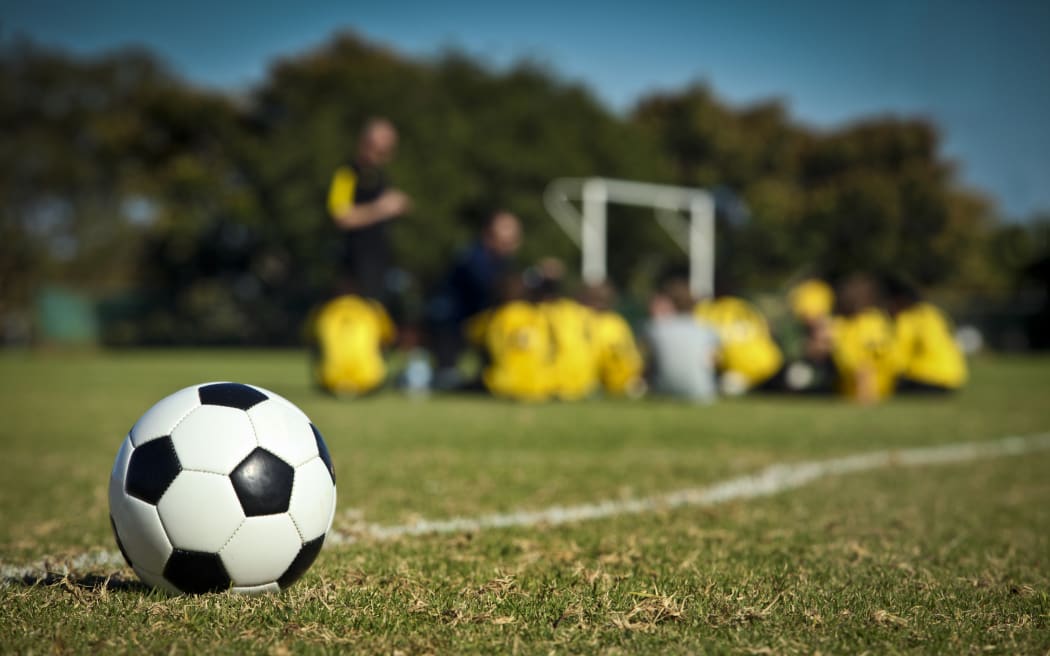 A soccer ball in the foreground, with a team of student players in the background.