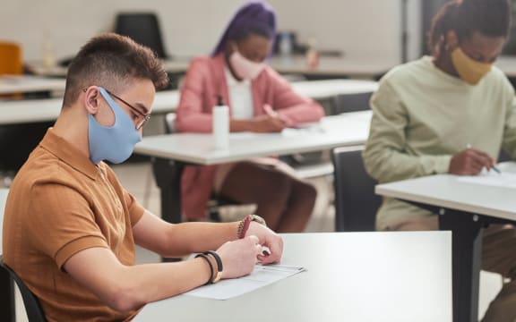 Side view portrait of young man wearing mask while taking test or exam in school with diverse group of people, copy space