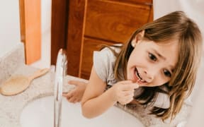 A young girl flosses her teeth at the bathroom sink.