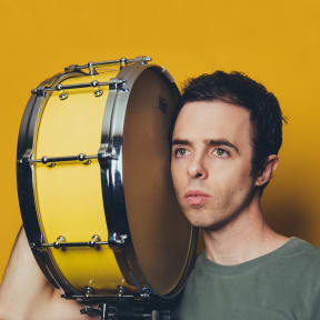 Publicity photo of American composer Daniel Temkin with a side drum on his shoulder.