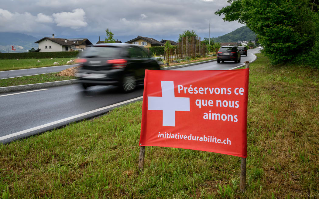 This photograph shows an election banner adorned with a Swiss cross reading in French “Let’s preserve what we love” beside a road ahead of the vote on the “No to 10 Million” immigration initiative, in Muraz on May 10, 2026. The “No to 10 million” immigration initiative proposed by the right-wing Swiss People’s Party, which aims to limit Switzerland’s permanent resident population to 10 million by 2050, will be put to a nationwide vote on June 14, 2026. (Photo by Fabrice COFFRINI / AFP)