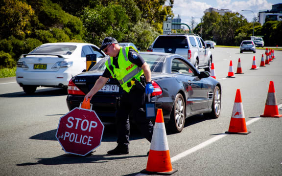A Queensland police officer moves a stop sign at a vehicle checkpoint on the Pacific Highway, along the state's border with New South Wales, in Brisbane on April 15, 2020.