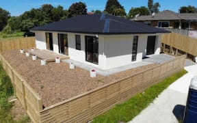A cream coloured house with a dark coloured roof and a wooden fence.