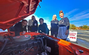 Mocketts Motors owner Chris Gudsell (left), automotive engineering apprentice Marco Shepherd, Hurunui Mayor Marie Black, and Hurunui District Council MTFJ Programme lead Chris Sutherland and MTFJ youth connector Anna Scott, look under the bonnet of Chris’s orange-and-black 1971 Valiant Pacer 3 speed, which can be spotted at the workshop when it is not at a car show.