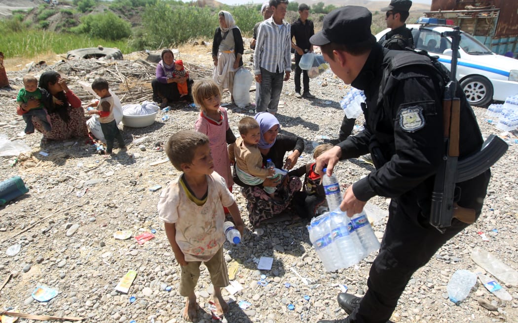 Peshmerga forces hand out water bottles to displaced Yizadi families from as they cross the Iraqi-Syrian border at the Fishkhabur crossing, in northern Iraq.
