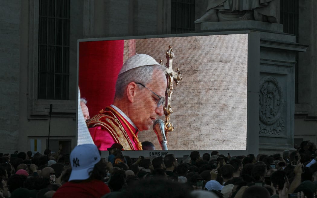 People watch a large screen as newly elected Pope Robert Francis Prevost, Pope Leo XIV, addresses the crowd from the main central loggia balcony of the St Peter's Basilica for the first time, after the cardinals ended the conclave, in The Vatican, on May 8, 2025. Robert Francis Prevost was on May 8, 2025 elected the first pope from the United States, the Vatican announced. A moderate who was close to Pope Francis and spent years as a missionary in Peru, he becomes the Catholic Church's 267th pontiff, taking the papal name Leo XIV. (Photo by Stefano Rellandini / AFP)
