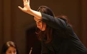 Conductor Simone Young holds her right hand out in front of her head as she conducts the orchestra.