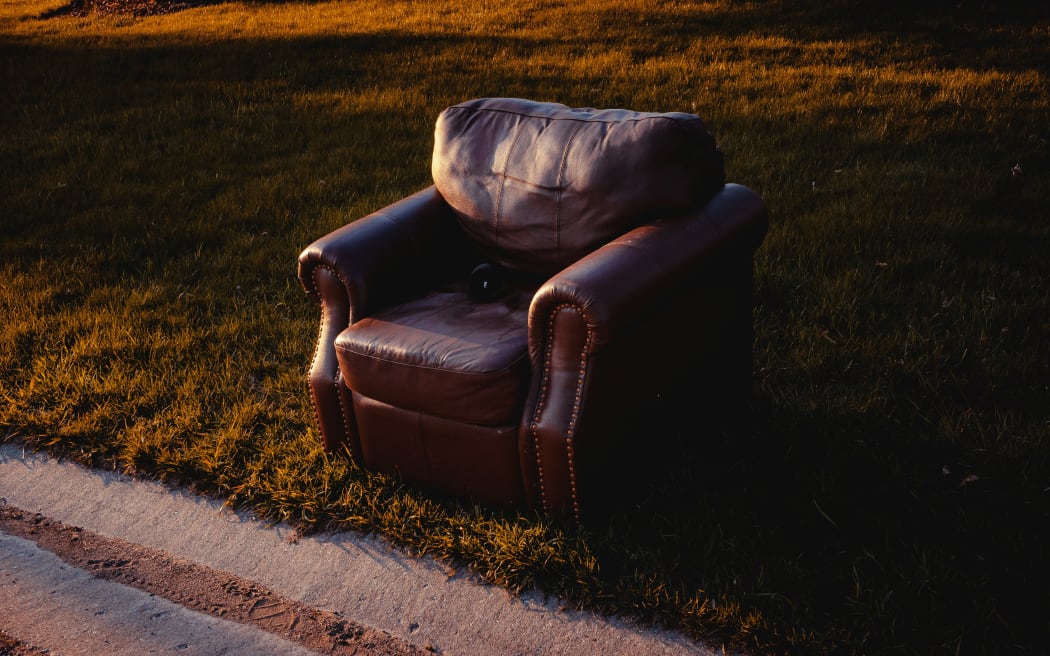 A leather couch chair thrown out on the side of the road.