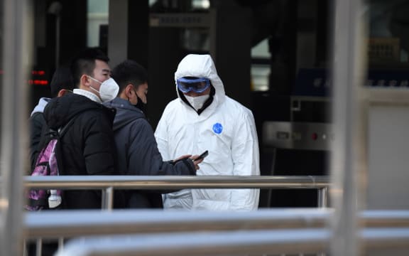 Passengers wearing protective facemasks are checked by security personnel wearing hazardous material suits at the entrance to the underground train station in Beijing on January 24, 2020, to help stop the spread of a deadly SARS-like virus which originated in the central city of Wuhan.