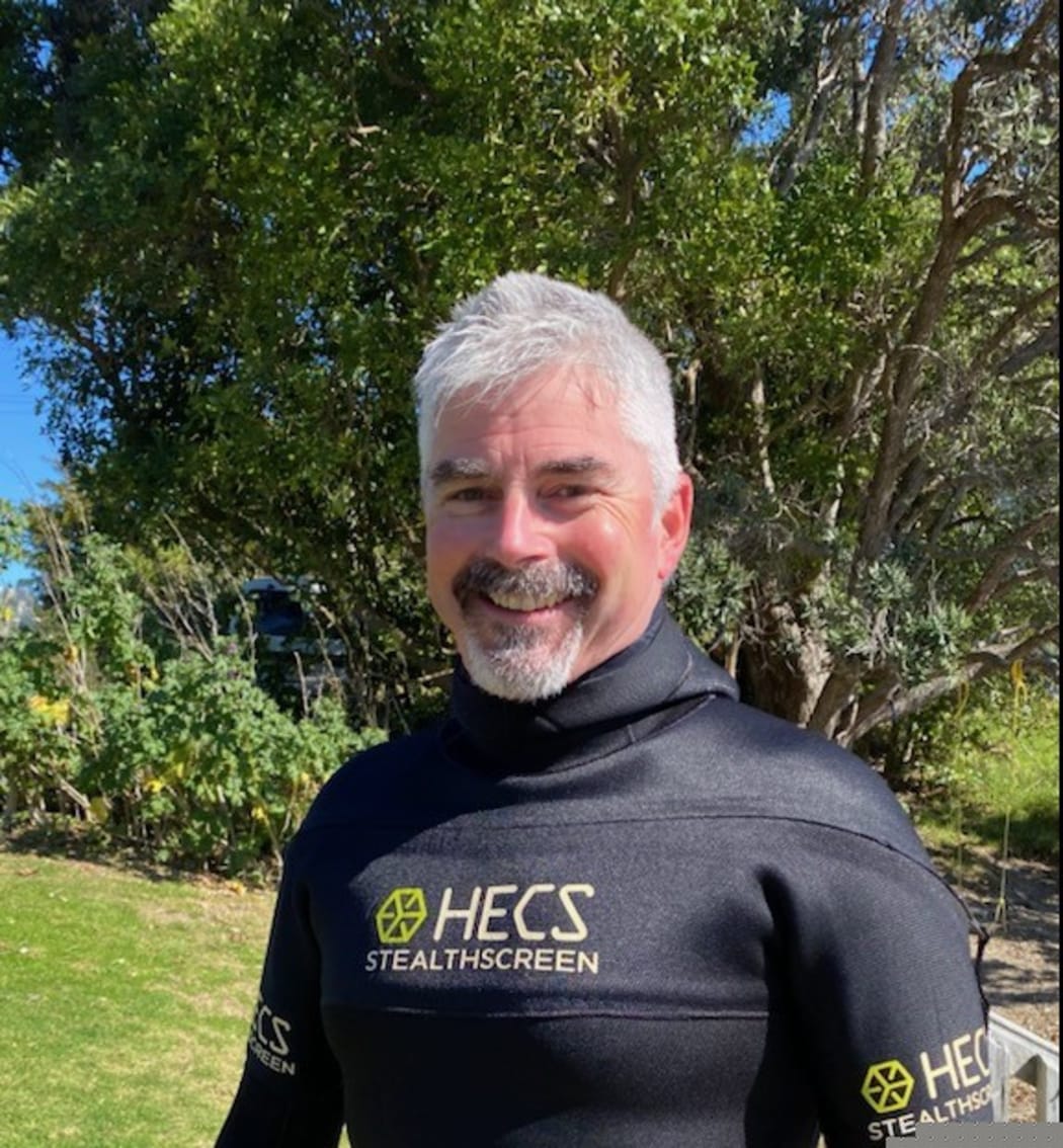 Craig smiles at the camera. He is wearing a wetsuit.