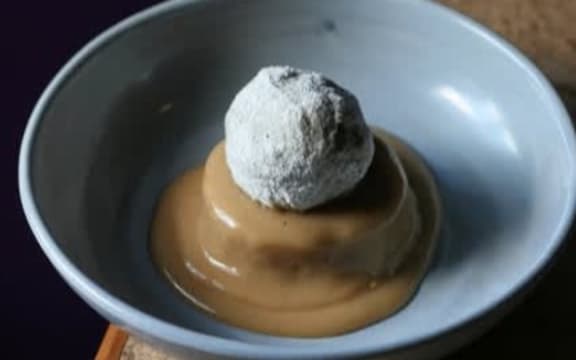 A bowl containing a sugary, deep fried feijoa on a bed of custard.