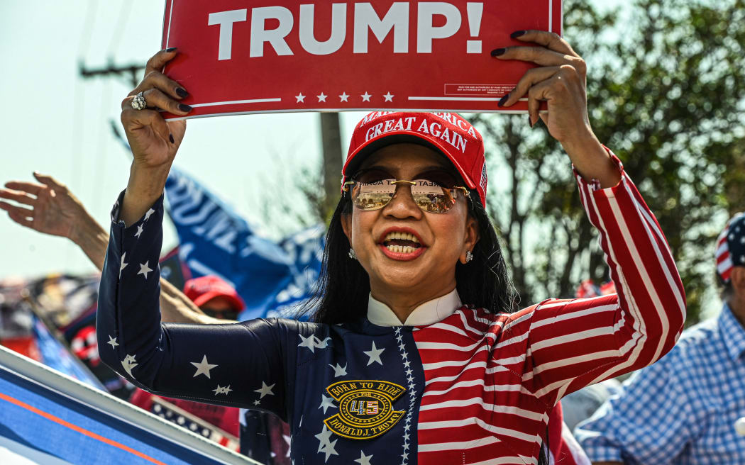 Ngoc Trang, a supporter of former US President Donald Trump, waits for the motorcade that will take him to Palm Beach International Airport in West Palm Beach, Florida, on April 3, 2023. - Former US President Donald Trump is to be booked, fingerprinted, and will have a mugshot taken at a Manhattan courthouse on the afternoon of April 4, 2023, before appearing before a judge as the first ever American president to face criminal charges.