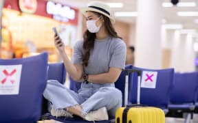 Asian young woman traveller wearing face maks using mobile phone at airport Due Covid-19 flu virus pandemic and protection