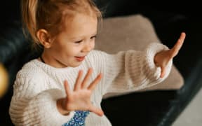 A small blonde girl holds up ten fingers while smiling.