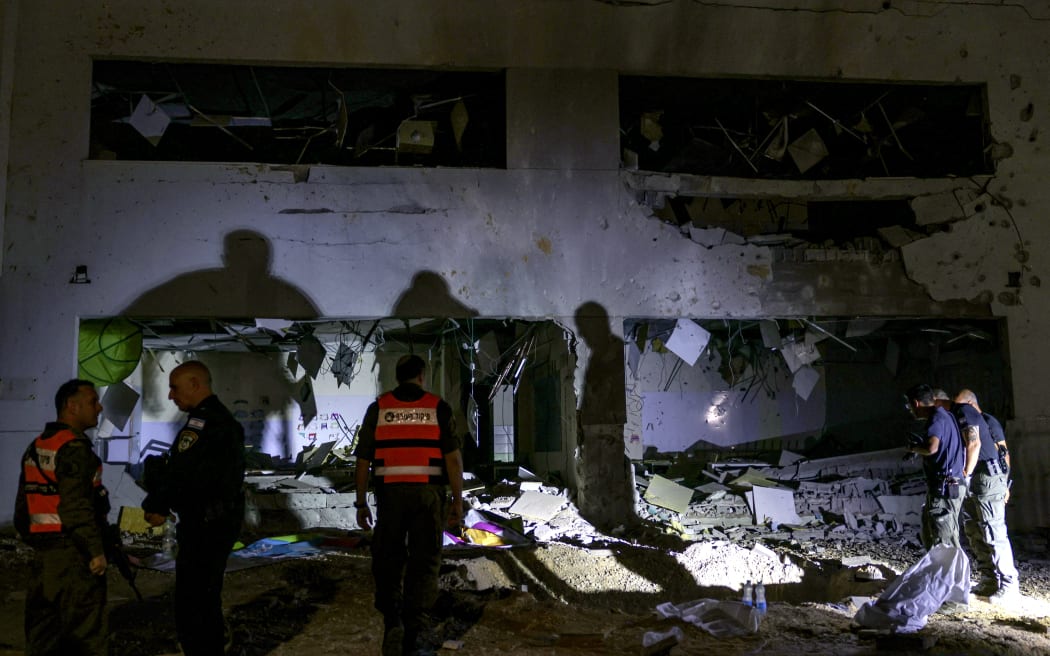 Members of Israel's Home Front Command and police forces inspect a crater left by an exploded projectile at a heavily-damaged school building in Israel's southern city of Gedera on October 1, 2024, after Iran launched a barrage of missiles at Israel in response to the killings of Lebanese Hezbollah leader Nasrallah and other Iran-backed militants. Reports said Iran fired between 150 and 200 missiles in the attack, the country's second on Israel after a missile and drone attack in April in response to a deadly Israeli air strike on the Iranian consulate in Damascus. (Photo by Menahem KAHANA / AFP)