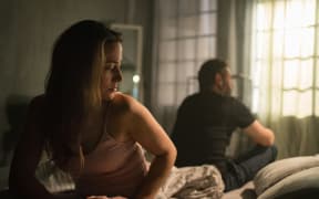 Couple in disagreement sit back to back on a bed.