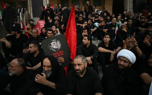 Men hold a placard calling for revenge against the US president as they gather to mourn Iran's slain supreme leader Ayatollah Ali Khamenei at the Grand Mosalla on the second day of funeral ceremonies in Tehran on 5 July 2026.